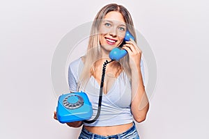 Young beautiful blonde girl holding vintage telephone looking positive and happy standing and smiling with a confident smile