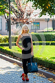 Young beautiful blonde girl posing on the background of the urban landscape. lady in a black dress and red shoes with a pleas