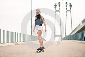 Young Beautiful Blonde Girl Riding Bright Skateboard on the Bridge