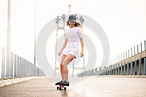 Young Beautiful Blonde Girl Riding Bright Skateboard on the Bridge