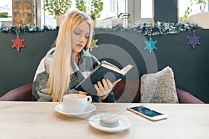 Young beautiful blonde girl sitting in coffee shop reading book