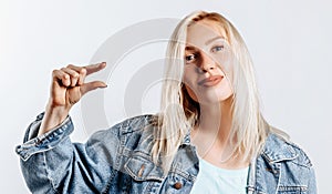 Young beautiful blonde girl standing over gray isolated background smiling and confident gesturing with hand doing small size sign