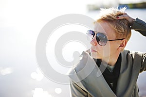 Young beautiful blonde girl sunbathing near the water. Wearing sunglasses. Outside