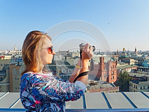Young beautiful blonde girl taking pictures of the city with a camera on a rooftop in Moscow, Russia.