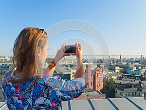 Young beautiful blonde girl taking pictures of the city with a smartphone on a rooftop in Moscow, Russia.