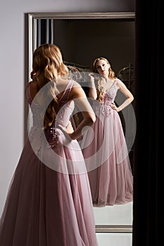 Young beautiful blonde girl wearing a full-length pink violet or purple chiffon prom ball gown decorated with sparkles