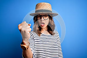 Young beautiful blonde girl wearing glasses and hat over blue isolated background annoyed and frustrated shouting with anger,