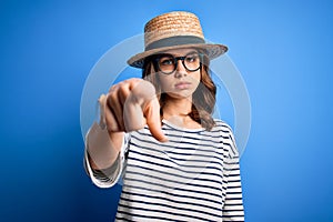 Young beautiful blonde girl wearing glasses and hat over blue isolated background pointing with finger to the camera and to you,