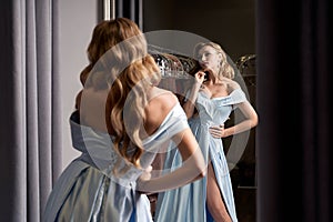 Young beautiful blonde girl wearing an off-the-shoulder full-length sky blue satin slit prom ball gown. Model looking in