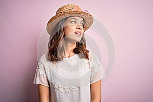 Young beautiful blonde girl wearing summer hat over pink isolated background looking away to side with smile on face, natural