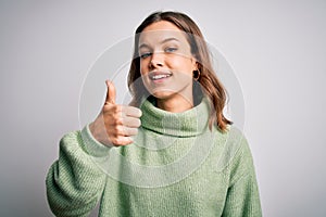 Young beautiful blonde girl wearing winter sweater standing over isolated background doing happy thumbs up gesture with hand