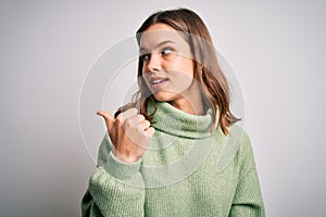 Young beautiful blonde girl wearing winter sweater standing over isolated background smiling with happy face looking and pointing