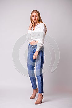 Young beautiful blonde girl in a white shirt. Studio gray isolated background