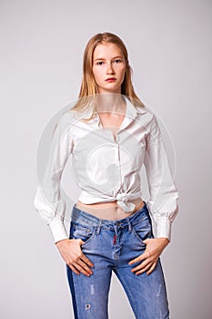 Young beautiful blonde girl in a white shirt. Studio gray isolated background