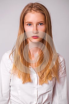 Young beautiful blonde girl in a white shirt. Studio gray isolated background