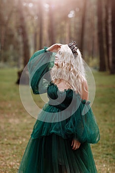 Young beautiful blonde hair woman queen. Princess walks. autumn green forest mystic. Vintage medieval shiny crown. Long evening