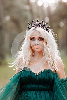 Young beautiful blonde hair woman queen. Princess walks. autumn green forest mystic. Vintage medieval shiny crown. Long evening