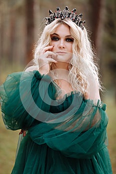 Young beautiful blonde hair woman queen. Princess walks. autumn green forest mystic. Vintage medieval shiny crown. Long evening