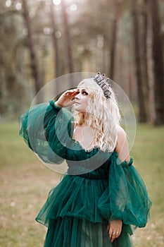 Young beautiful blonde hair woman queen. Princess walks. autumn green forest mystic. Vintage medieval shiny crown. Long evening