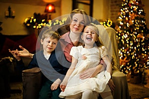 Young beautiful blonde mom with two children posing in armchair in christmas interior