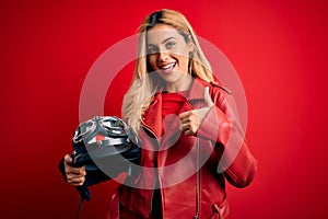 Young beautiful blonde motorcyclist woman holding moto helmet over isolated red background happy with big smile doing ok sign,