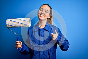 Young beautiful blonde painter woman with blue eyes painting wearing uniform using roller happy with big smile doing ok sign,