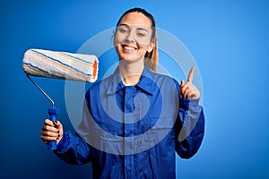 Young beautiful blonde painter woman with blue eyes painting wearing uniform using roller surprised with an idea or question