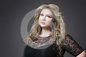 Young beautiful blonde plus size model in black dres, xxl woman portrait on gray studio background