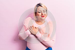 Young beautiful blonde plus size woman wearing casual sweater over isolated pink background smiling with hands on chest, eyes