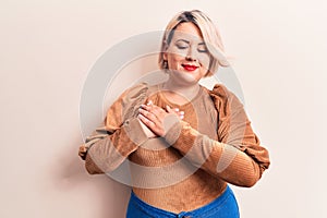 Young beautiful blonde plus size woman wearing casual sweater over isolated white background smiling with hands on chest, eyes