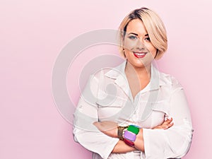 Young beautiful blonde plus size woman wearing elegant shirt over isolated pink background happy face smiling with crossed arms