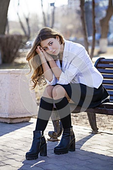 Young beautiful blonde schoolgirl sitting on a bench