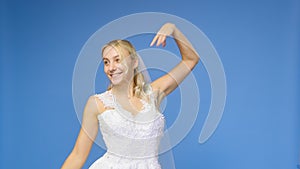 Young beautiful blonde smiling in a wedding white dress and veil on a blue background. The girl looks into the camera