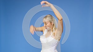 Young beautiful blonde smiling in a wedding white dress and veil on a blue background. The girl looks into the camera