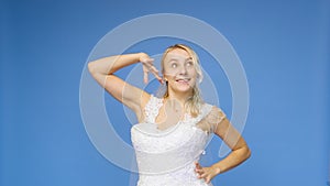 Young beautiful blonde smiling in a wedding white dress and veil on a blue background. The girl looks into the camera