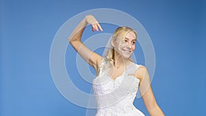 Young beautiful blonde smiling in a wedding white dress and veil on a blue background. The girl looks into the camera