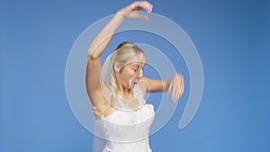 Young beautiful blonde smiling in a wedding white dress and veil on a blue background. The girl looks into the camera