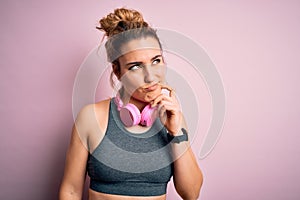 Young beautiful blonde sportswoman wearing sportswear listening to music using headphones with hand on chin thinking about