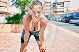 Young beautiful blonde sporty girl exhausted with hands on knees resting at street of city