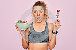 Young beautiful blonde sporty woman with blue eyes holding bowl with healthy salad scared in shock with a surprise face, afraid