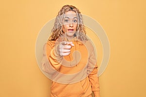 Young beautiful blonde sporty woman wearing casual sweatshirt over yellow background pointing displeased and frustrated to the
