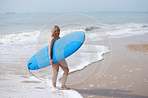 Young and beautiful blonde surfer woman in pink bikini and blue surfboard. The girl enjoys her holidays on the beach to practice