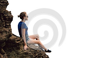 Young beautiful blonde tourist girl sits on a rocky ledge of a rock and looks far into the distance in the early foggy morning.