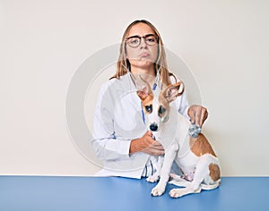 Young beautiful blonde veterinarian woman checking dog health using stethoscope depressed and worry for distress, crying angry and