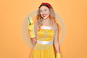 Young beautiful blonde woman with blue eyes cleaning using gloves and cleaner scourer with a happy face standing and smiling with