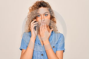 Young beautiful blonde woman with blue eyes having conversation talking on the smartphone cover mouth with hand shocked with shame