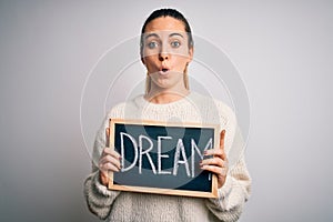 Young beautiful blonde woman with blue eyes holding blackboard with dream word message scared in shock with a surprise face,