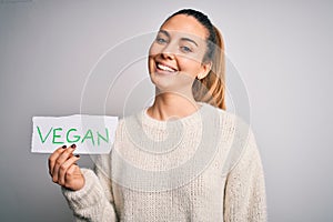 Young beautiful blonde woman with blue eyes holding paper with vegan message with a happy face standing and smiling with a