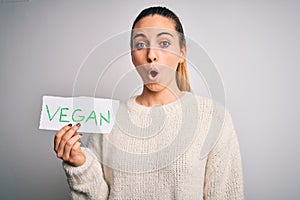 Young beautiful blonde woman with blue eyes holding paper with vegan message scared in shock with a surprise face, afraid and