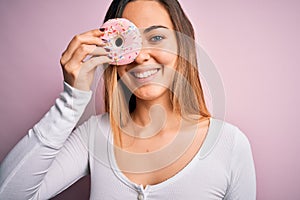 Young beautiful blonde woman with blue eyes holding pink doughnut over isolated background with a happy face standing and smiling